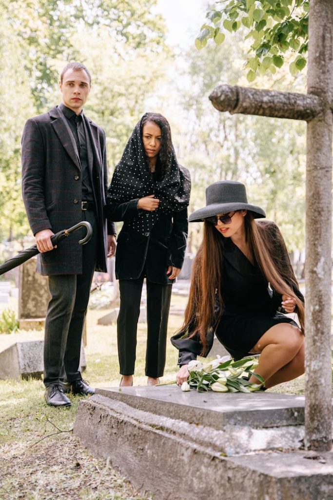a-family-wearing-black-clothes-while-standing-near-the-gravestone-8963852 A group of adults dressed in black pay their respects at a cemetery, symbolizing grief and remembrance.